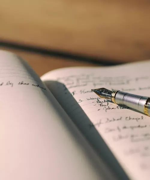 Nærbilde av en notatbok hvor det er skrevet tekst i, med en penn liggende oppå notatboka.