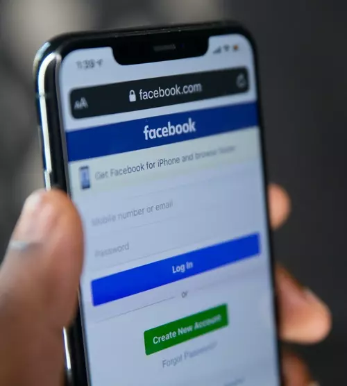 En mobil blir holdt opp og viser Facebook logg inn side.