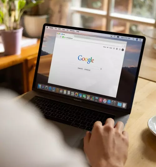 En person sitter med ryggen til og har åpnet Google søkefelt på sin bærebare datamaskin.