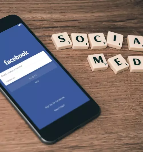 En mobil ligger på et bord og har åpnet Facebook appen. Det ligger bokstaver ved siden av mobilen hvor det står skrevet Social Media (sosiale medier på norsk).