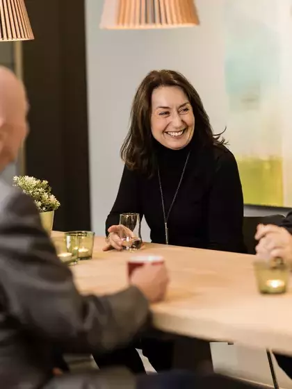 Bilde av tre smilende ansatte som sitter ved et bord og snakker